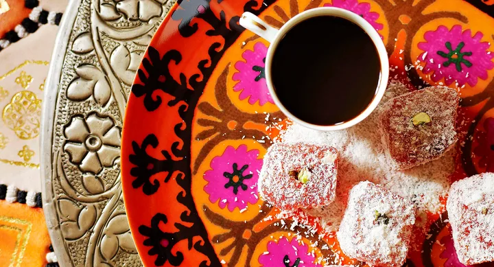 Cup of coffee and Turkish delight on a colorful, decorative plate with designs and patterns.