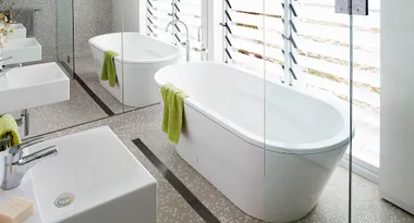 Modern bathroom with a white freestanding bathtub, green towel, sink, and tiled floor.