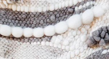 Close-up of a textured woven fabric in white and gray with assorted patterns and large yarn bubbles.
