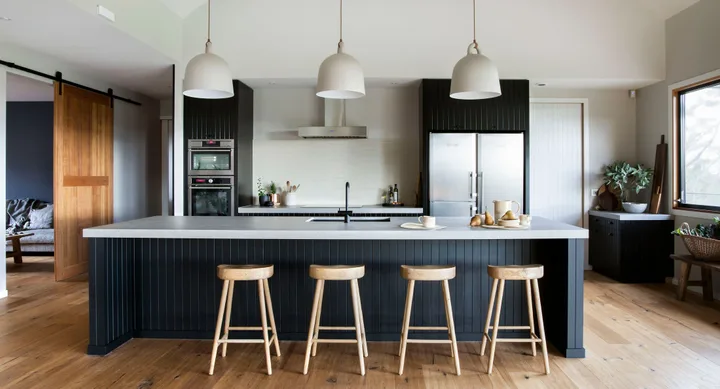 Modern kitchen with black cabinetry, a large island, light wood stools, pendant lights, and stainless steel appliances.