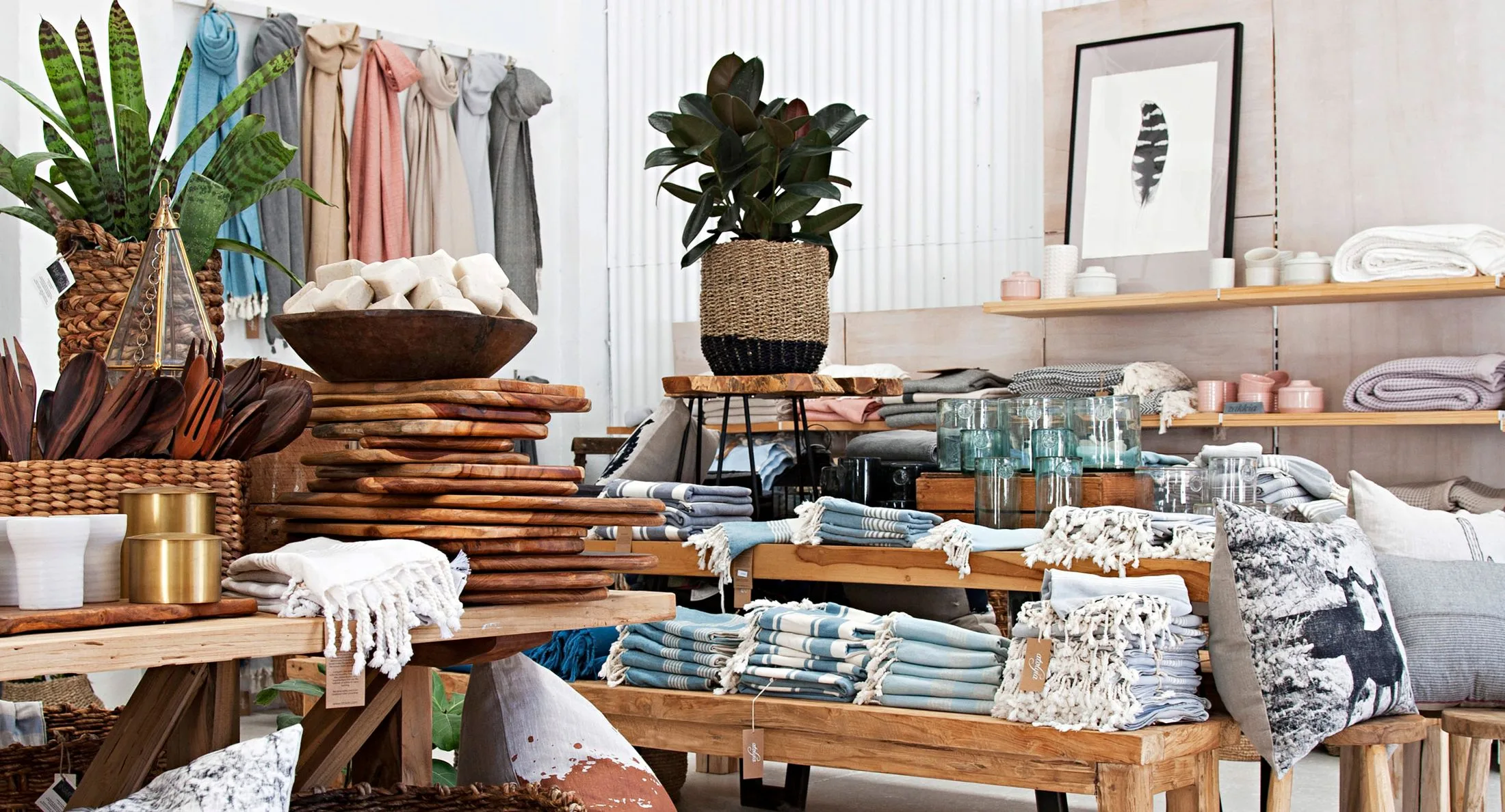 Store display with wooden boards, textiles, plants, and home decor items on tables and shelves in a cozy, rustic setting.