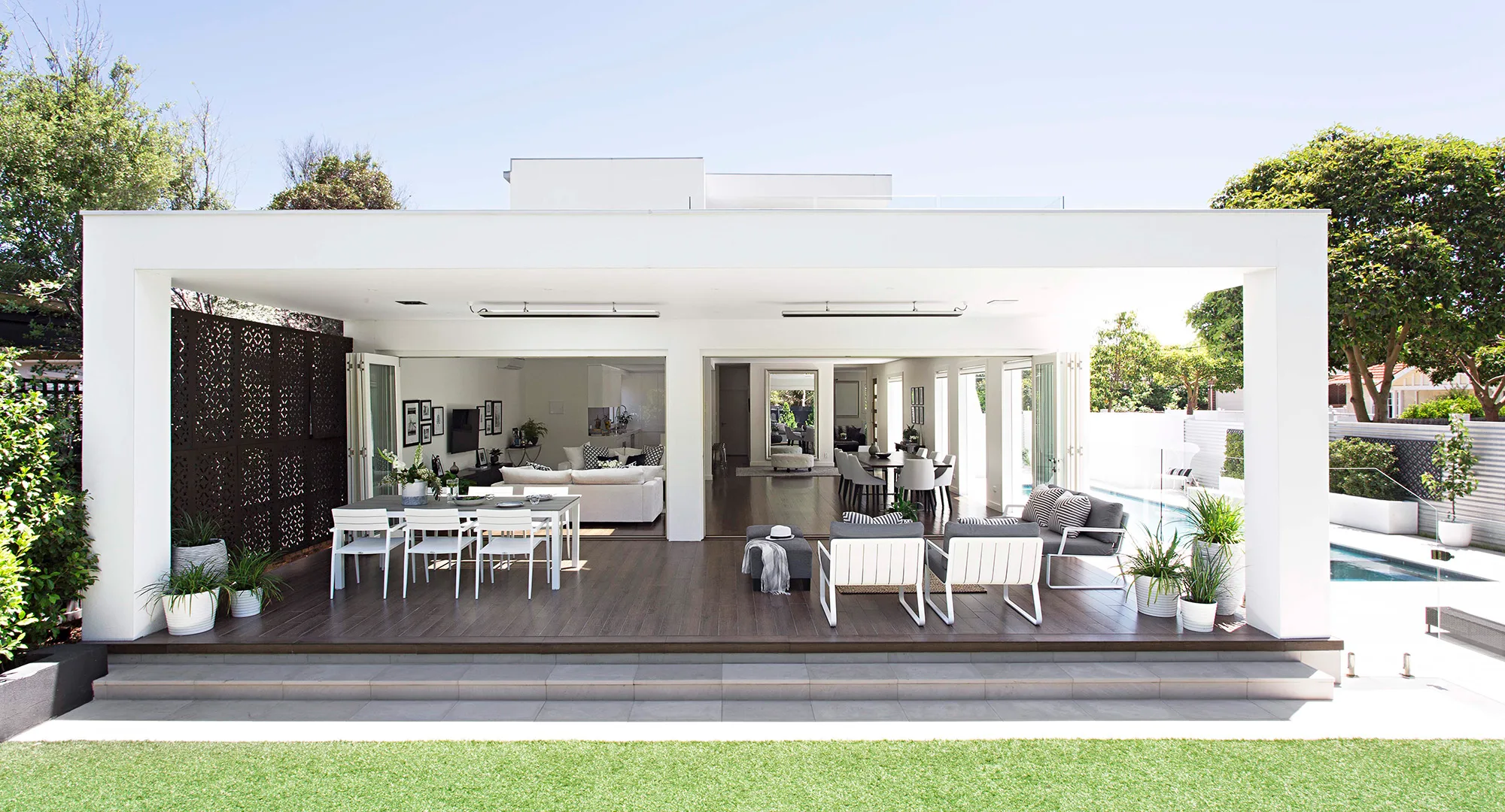 Outdoor patio with sleek modern furniture, covered seating area, open view to pool, and lush greenery surrounding the space.