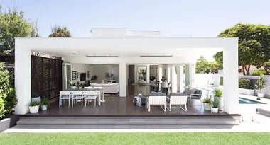 Outdoor patio with sleek modern furniture, covered seating area, open view to pool, and lush greenery surrounding the space.
