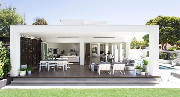 Outdoor patio with sleek modern furniture, covered seating area, open view to pool, and lush greenery surrounding the space.