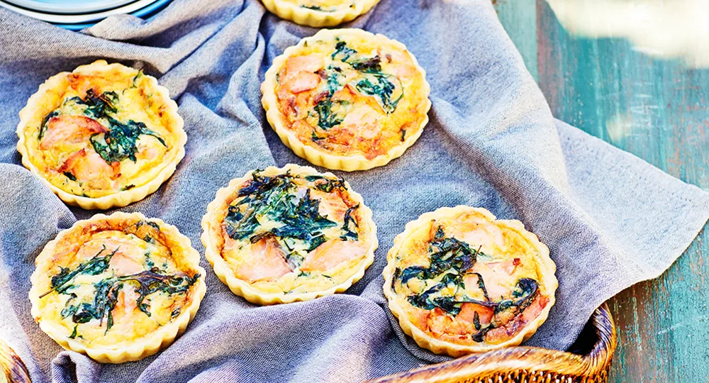 Mini quiches with spinach and ham on cloth in a basket.
