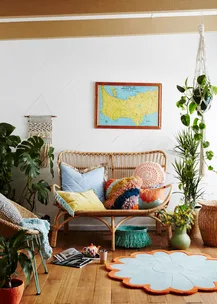 Cozy living room with a rattan sofa, colorful pillows, wall map, and potted plants on a wooden floor.