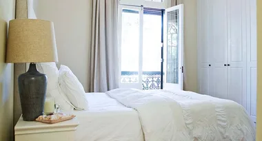 Cozy bedroom with white bedding, a bedside table with a lamp, and an open door leading to a balcony.
