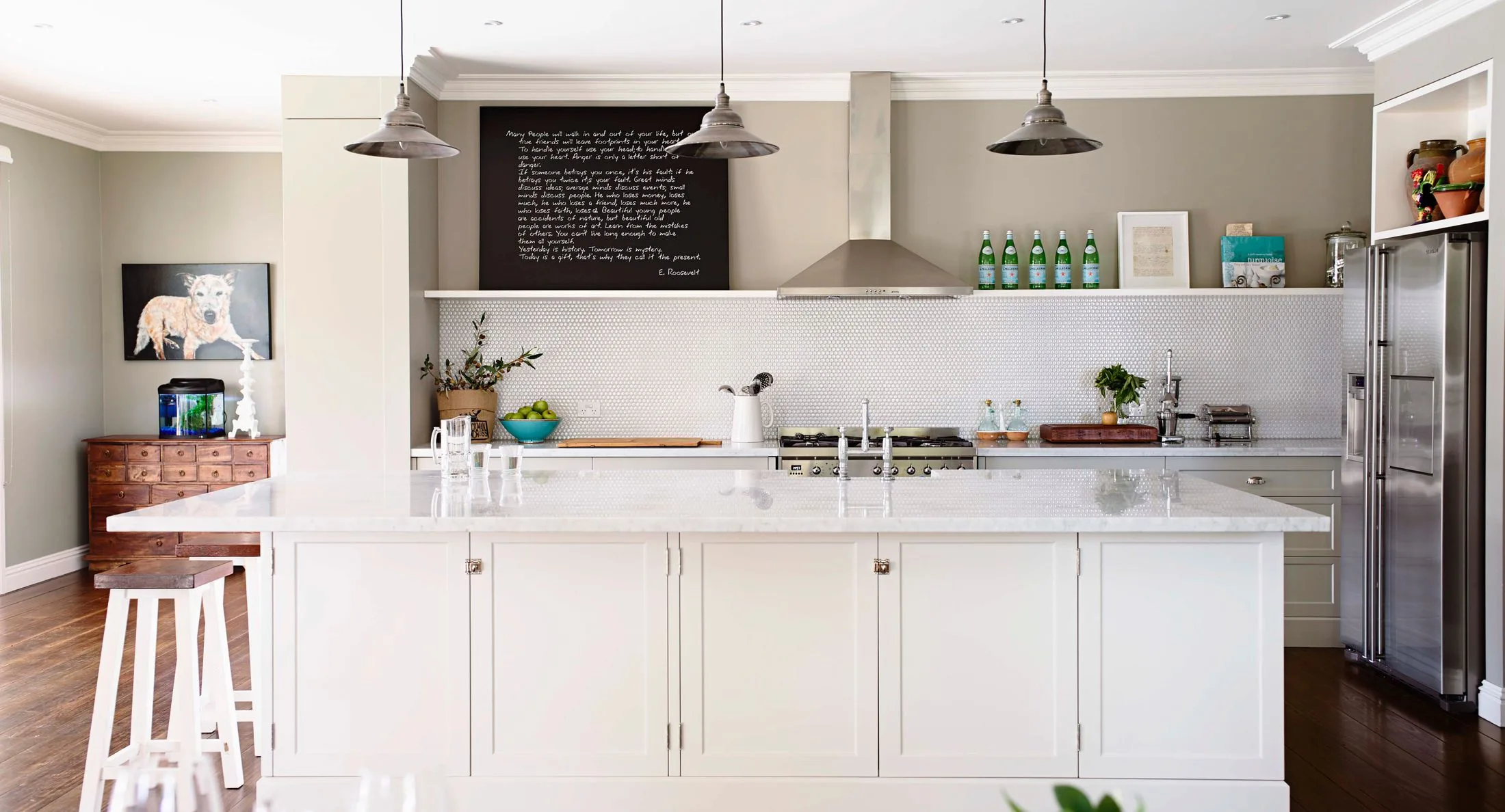 Modern kitchen with white island, pendant lights, art, and plants; organized and stylish decor.
