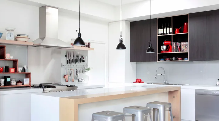 Modern kitchen with a large island, hanging lights, and bar stools. Shelves and counter hold various utensils and decor.