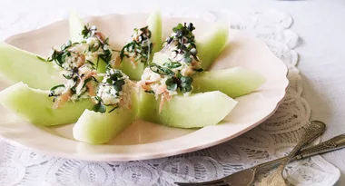 Melon slices topped with crab and garnish on a decorative plate with cutlery.