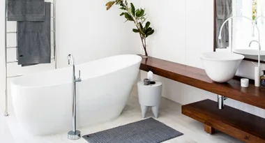 Modern bathroom with a freestanding tub, wooden vanity, round basin, grey towels, and a plant on the shelf.