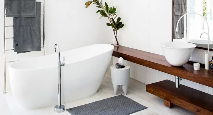 Modern bathroom with a freestanding tub, wooden vanity, round basin, grey towels, and a plant on the shelf.
