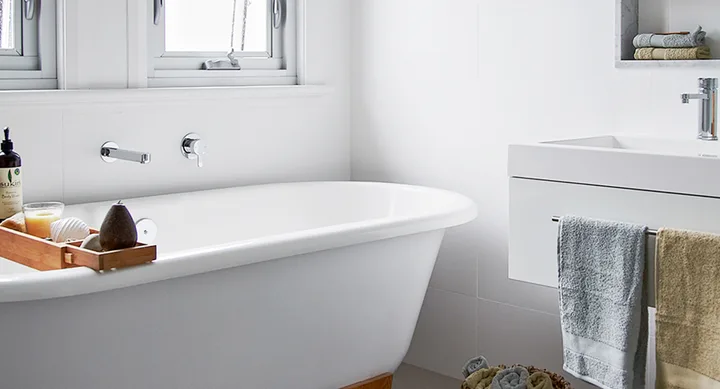 A clean, modern bathroom with a white freestanding bathtub, towels, and bath accessories on a wooden rack.
