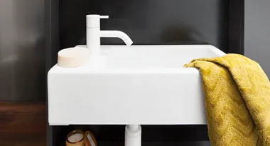 White sink with modern faucet, a round soap, and a yellow towel draped on the side. Dark background.