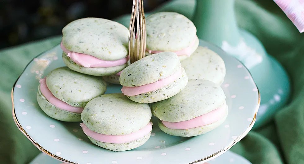 Mint green macarons with pink filling on a pastel polka-dot plate, arranged on a tiered stand.