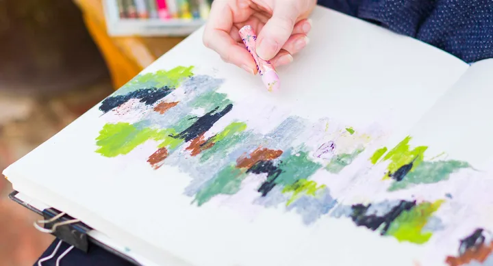Person sketching abstract colors in a notebook with a pastel.