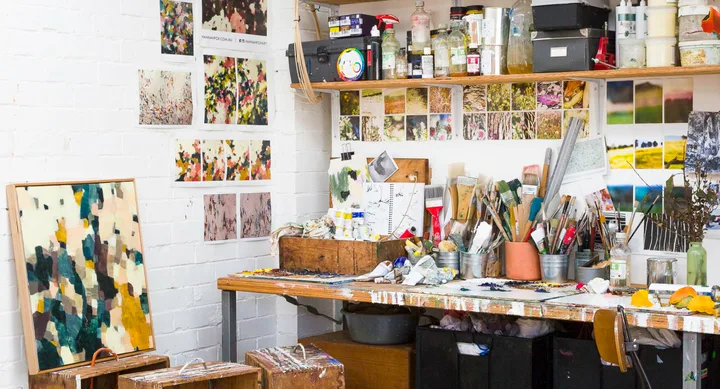 Artist's studio with paintbrushes, color palettes, and abstract artwork on wall and table, Hannah Fox art space.