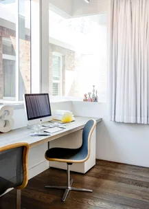 Bright home office with a computer, modern chair, decor items on desk by large window and white curtains.