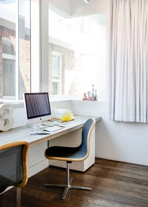 Bright home office with a computer, modern chair, decor items on desk by large window and white curtains.