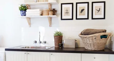 Laundry room with sink, shelves, framed art, and wicker basket with towels.