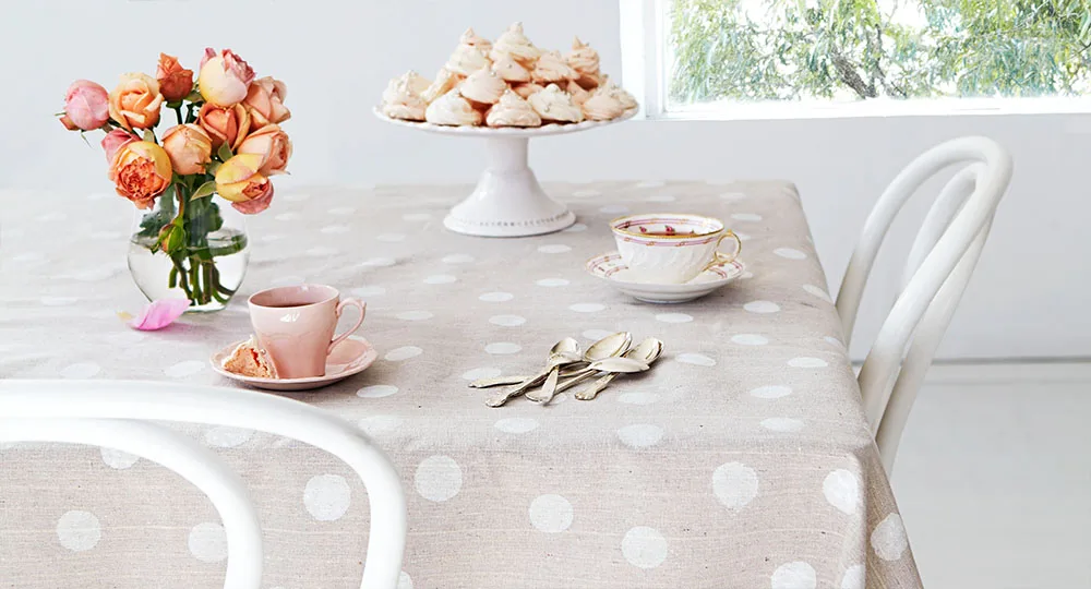 A polka dot tablecloth with roses, a pink teacup, a floral saucer, and a cake stand with meringues.