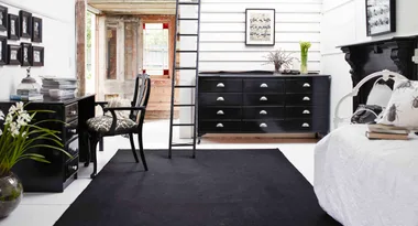 Modern black and white bedroom, desk, and chair, with ladder, dresser, and minimal decor.