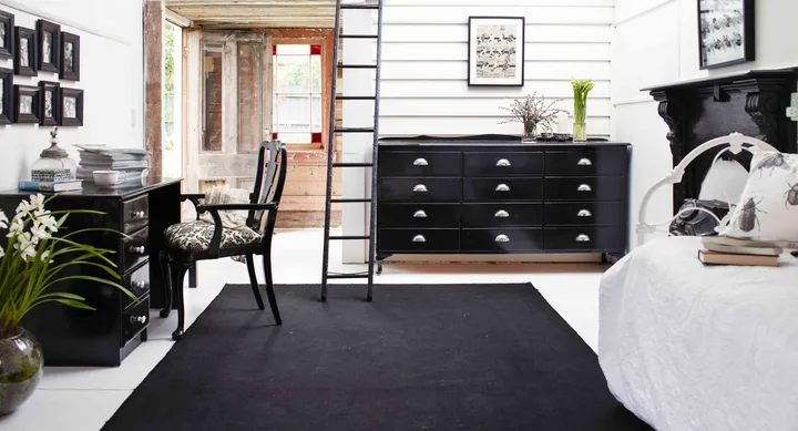 Modern black and white bedroom, desk, and chair, with ladder, dresser, and minimal decor.