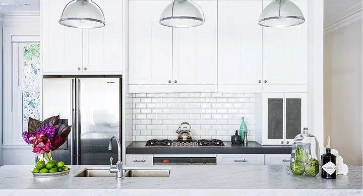 Modern kitchen with white cabinets, marble countertops, stainless steel appliances, flowers, and green limes.