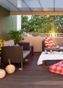 Outdoor patio with wicker chairs, plants, a table with wine glasses, and patterned red and white cushions.