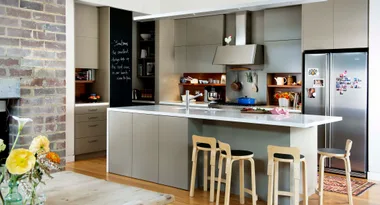 Modern kitchen with an island, bar stools, stainless steel appliances, and a chalkboard wall.