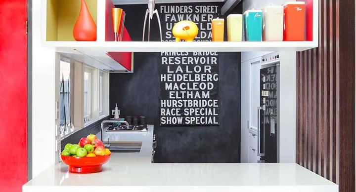 Bright kitchen with colorful jars, fruit bowl, black wall with white text, and modern appliances.