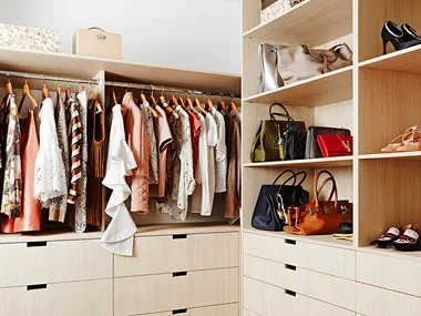 Spacious walk-in closet with clothes on hangers, handbags, and shoes neatly arranged on shelves and drawers.