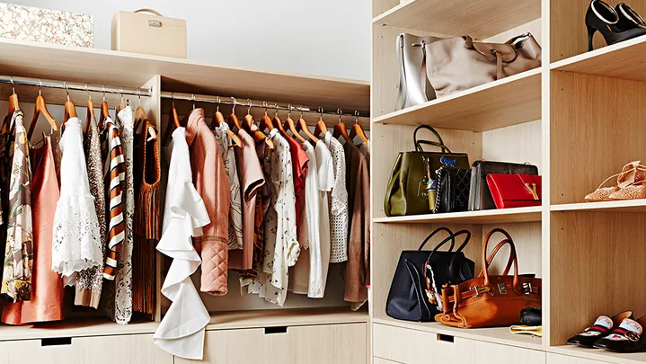 Spacious walk-in closet with clothes on hangers, handbags, and shoes neatly arranged on shelves and drawers.