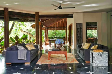 Stylish living room with dark sofas, patterned cushions, wooden decor, and lush greenery outside.