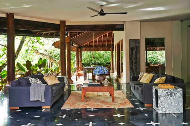 Stylish living room with dark sofas, patterned cushions, wooden decor, and lush greenery outside.