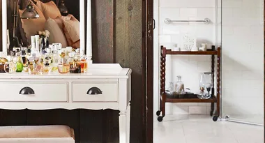 Dressing table with various bottles and mirrors in a cozy room with wooden and white tile decor.