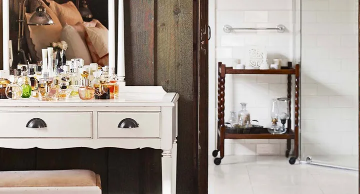 Dressing table with various bottles and mirrors in a cozy room with wooden and white tile decor.