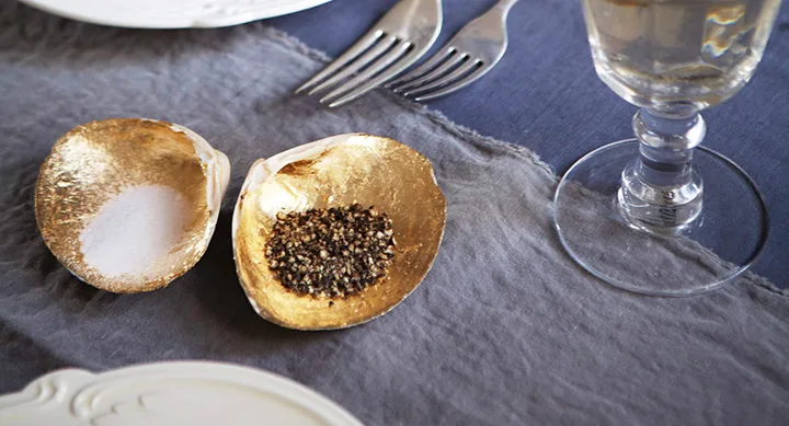 Golden oyster shells used as salt and pepper holders on a table setting.