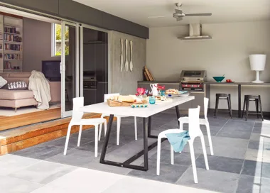 Modern open-plan kitchen with a dining table set for lunch, featuring white chairs and sliding doors to a cozy living area.