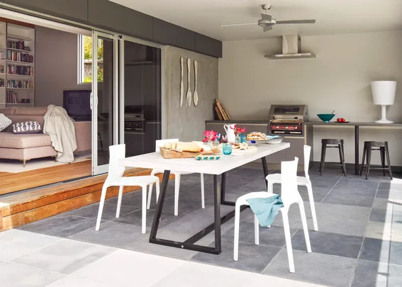 Modern open-plan kitchen with a dining table set for lunch, featuring white chairs and sliding doors to a cozy living area.