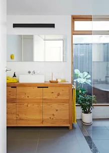 Bright bathroom with wooden vanity, white sink, mirror, potted plant, and window, creating a natural, airy atmosphere.