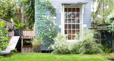 A small backyard with a climbing vine, white roses, a metal slide, and pendant lights.