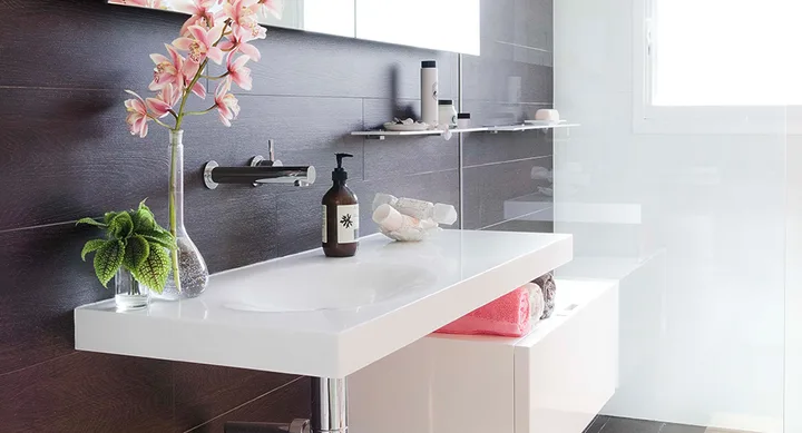 Modern bathroom with dark wood wall, white sink, pink flowers, and toiletries.