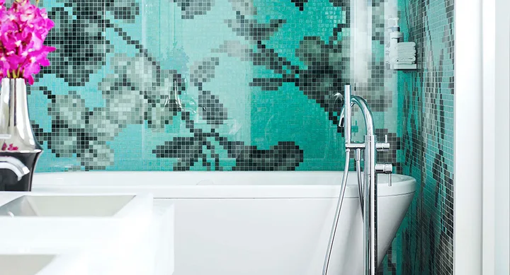 Modern bathroom with a white tub, floral mosaic turquoise tiles, chrome faucet, and pink flowers in a vase.