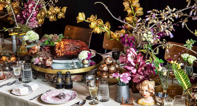 Opulent dining table with glazed ham, flowers, ornate plates, and vintage decorations.