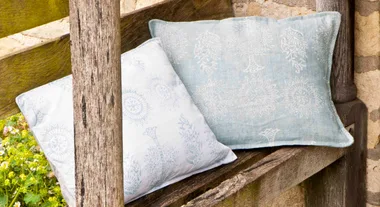 Two patterned cushions on a wooden bench with a stone wall backdrop.