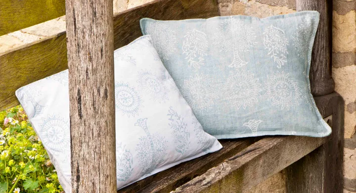 Two patterned cushions on a wooden bench with a stone wall backdrop.