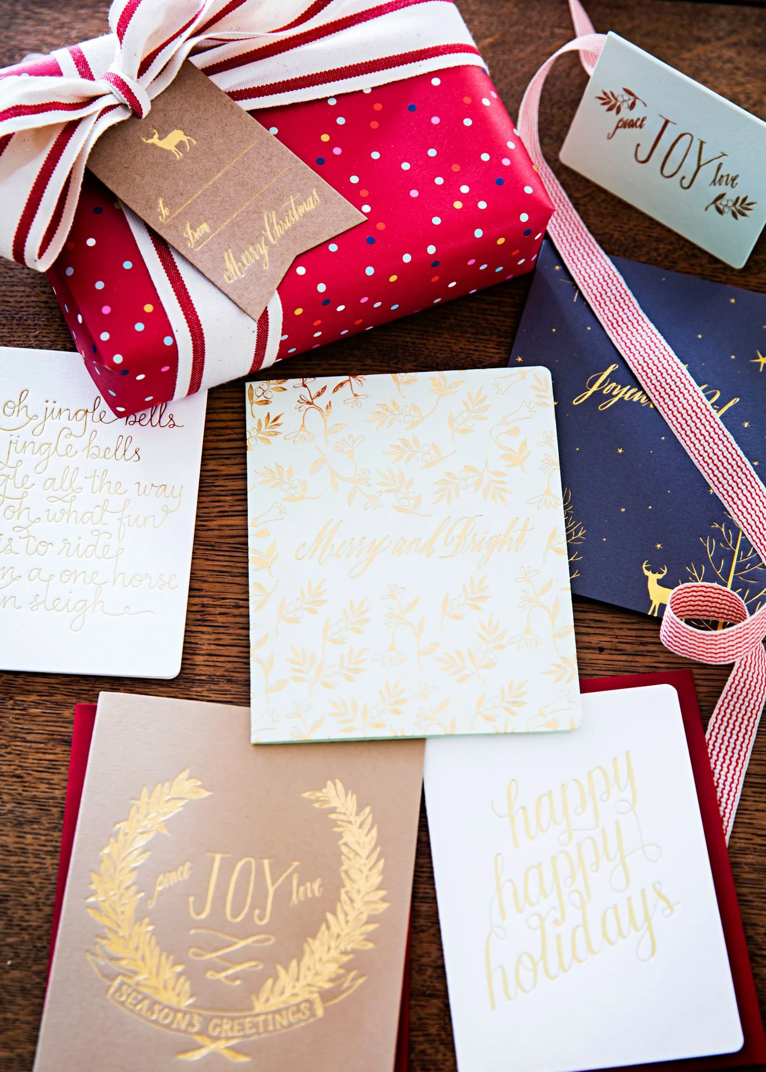 Gift wrapped in red polka dot paper with holiday cards saying "Merry Christmas" and "Joy."