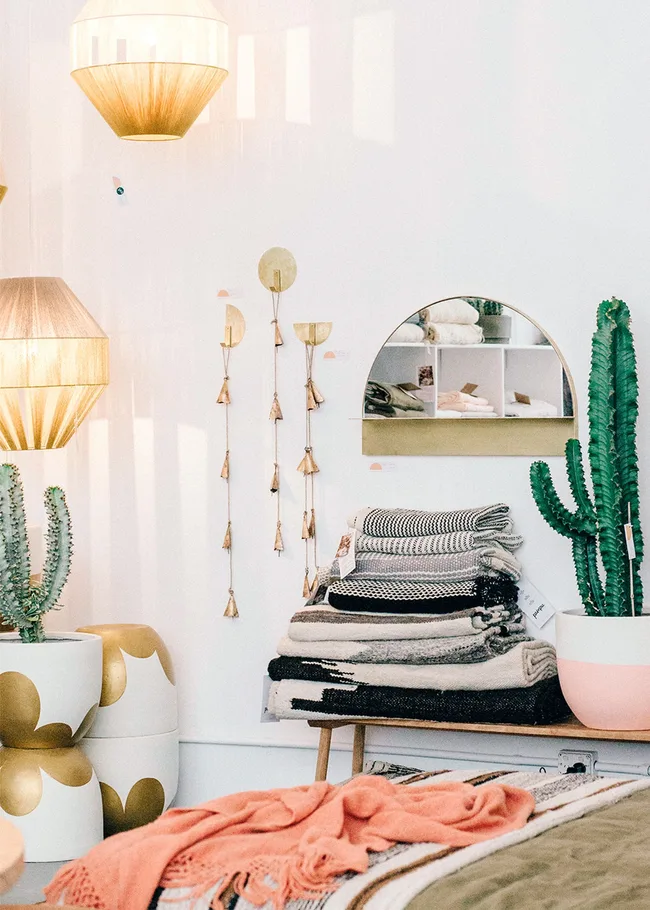 Cozy room with cacti, warm lighting, stacked blankets, and a mirror reflecting shelves.