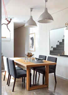 Modern dining room with wooden table, black chairs, pendant lights, wall art, and mannequin on red string.
